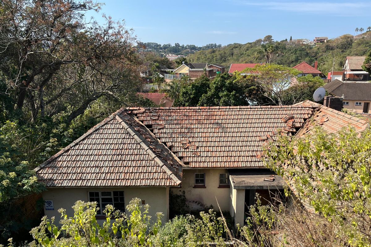 Aerial view of a residential property showing significant damage to the tiled roof structure and overgrown surrounding vegetation.