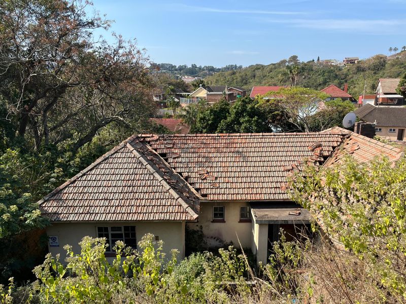 Aerial view of a residential property showing significant damage to the tiled roof structure and overgrown surrounding vegetation.