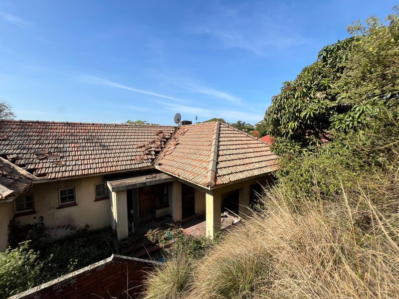 Rear view of a house showing significant roof tile damage and overgrown garden areas requiring maintenance and structural repair.