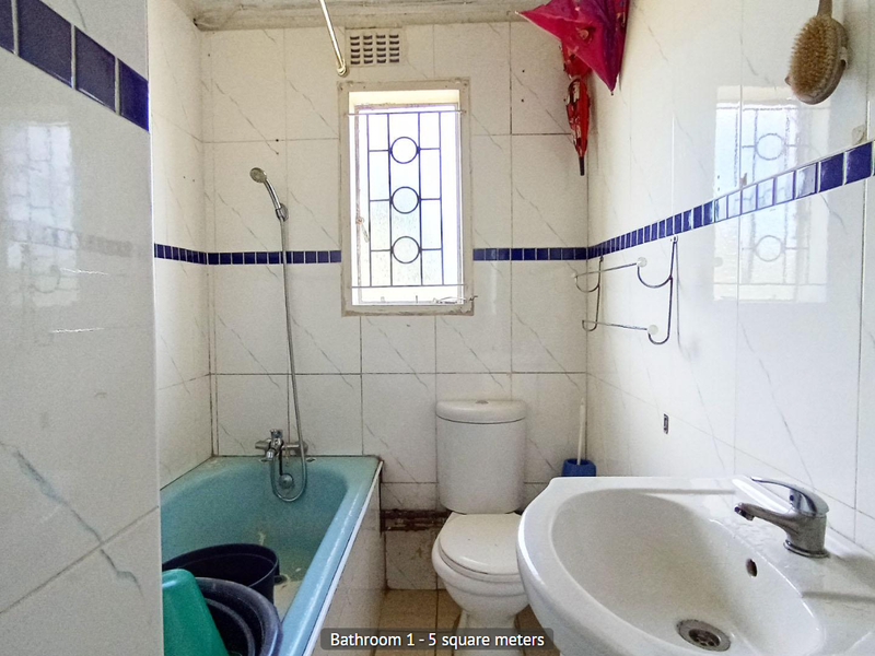 A compact bathroom featuring a blue bathtub, pedestal basin, and toilet, with white wall tiles and blue accent detailing.