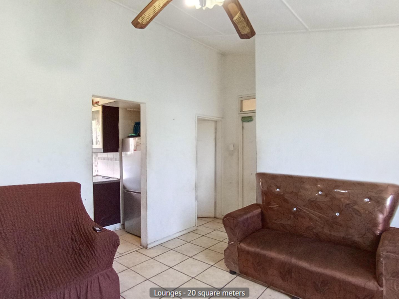 A living room area featuring ceramic floor tiles and a ceiling fan, providing access to the kitchen and adjacent rooms.