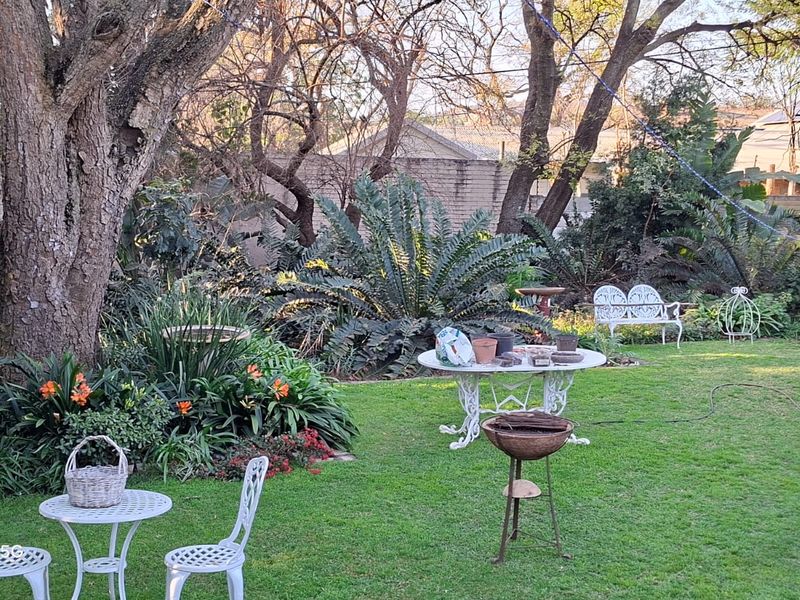 A lush, well-established garden featuring mature trees, manicured lawn, and perimeter boundary walls, providing a private and serene outdoor setting.
