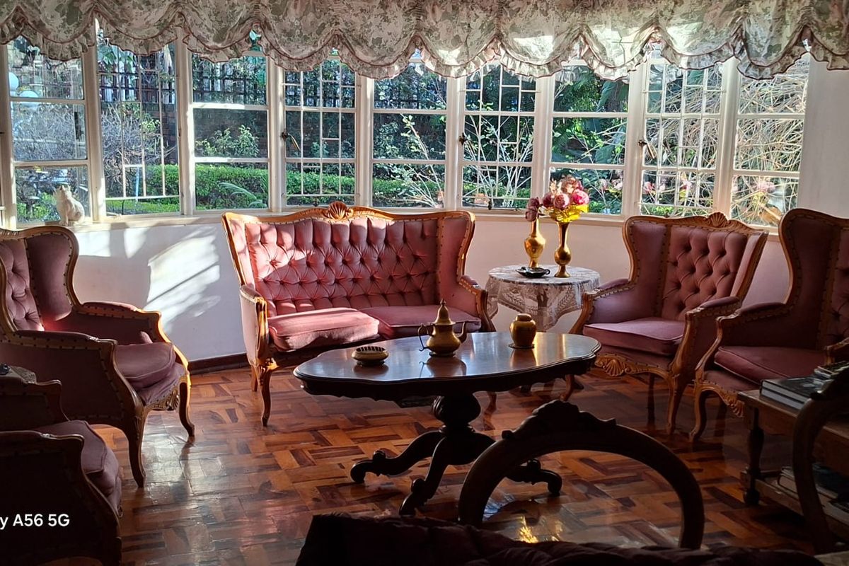 A sunlit living room featuring classic parquet flooring and a large bay window with leaded glass detailing, offering views of the garden.