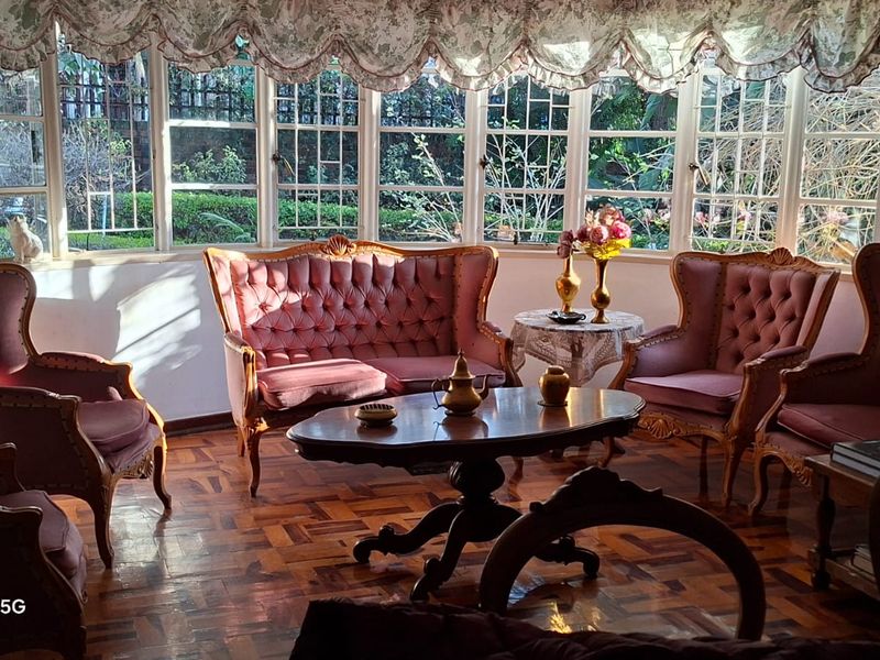 A sunlit living room featuring classic parquet flooring and a large bay window with leaded glass detailing, offering views of the garden.