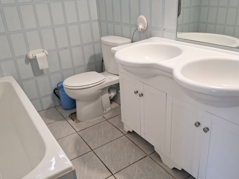 A functional bathroom featuring a double vanity, built-in bathtub, and toilet with light blue tiled walls and neutral floor tiles.