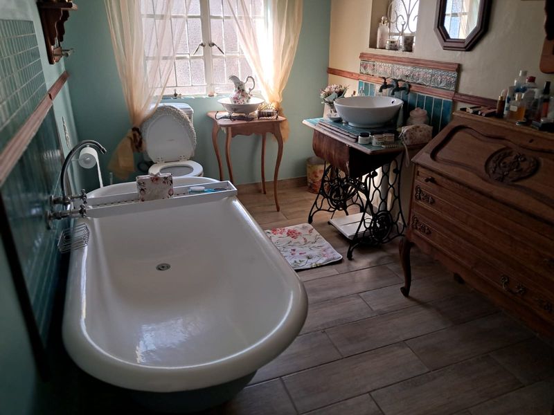 A characterful bathroom featuring a freestanding bathtub, wall-mounted fixtures, and a unique vanity setup with tiled splashbacks and wood-look flooring.