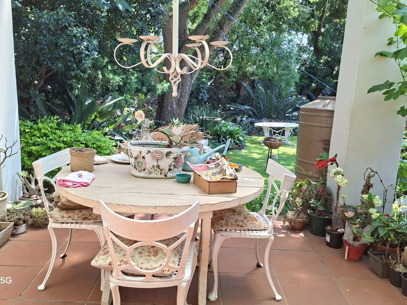 A covered outdoor patio area featuring tiled flooring and a hanging light fixture, overlooking a lush garden space.