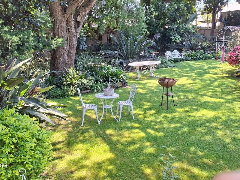 A lush, well-maintained garden featuring mature trees, established landscaping, and a spacious lawn area.
