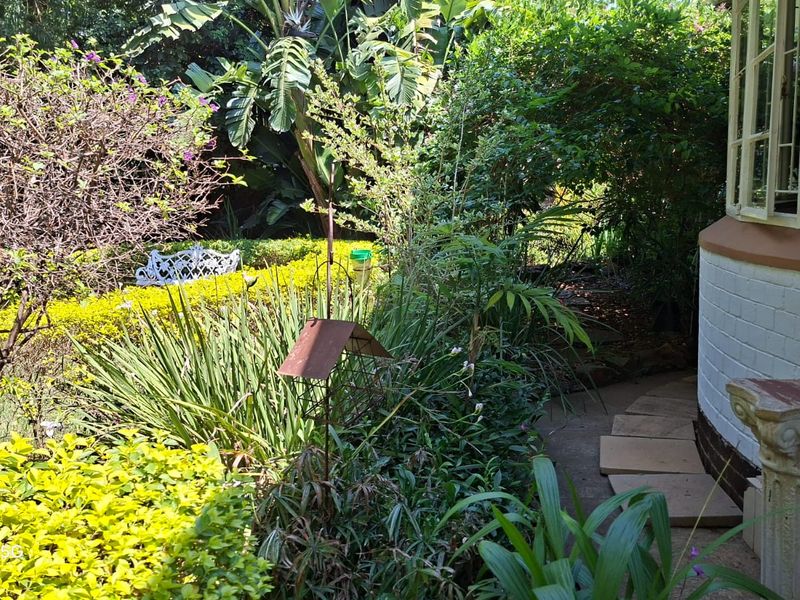A lush, established garden area featuring a stone pathway leading alongside a bay window of the house.