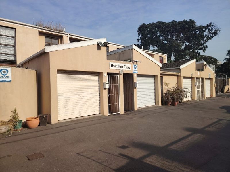 Front elevation of a townhouse complex featuring multiple garage units with roller shutter doors and security access gates.