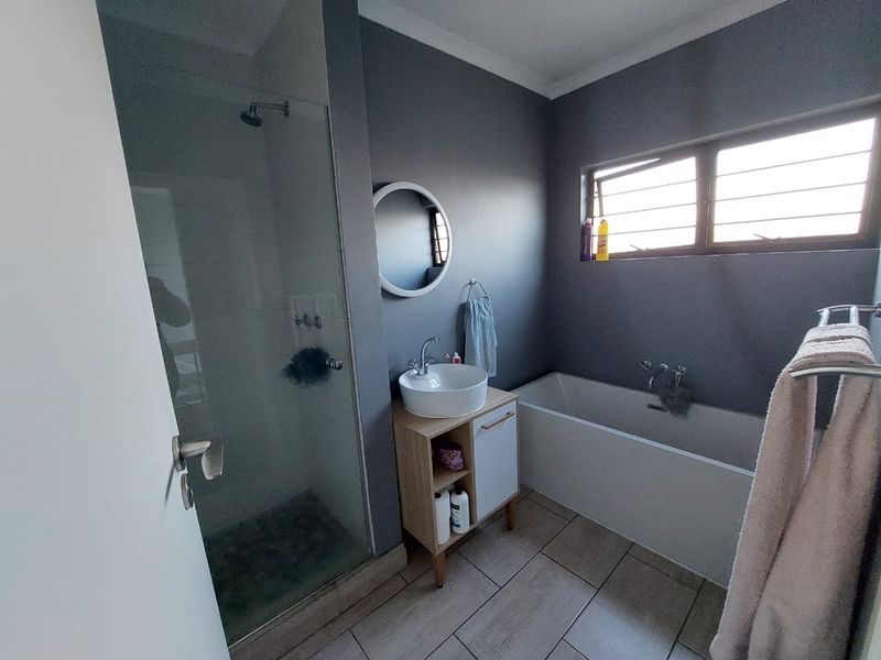 Modern bathroom featuring a glass-enclosed shower, a separate bathtub, a vanity with a vessel sink, and neutral floor tiling.