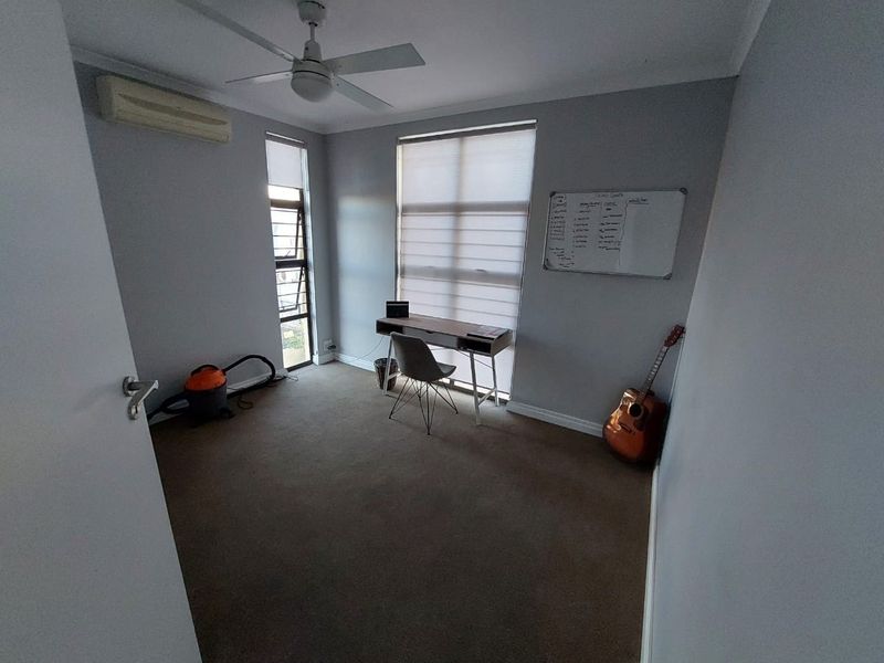 A functional bedroom featuring carpet flooring, a ceiling fan, and a wall-mounted split-system air conditioner, providing a comfortable and versatile living space.