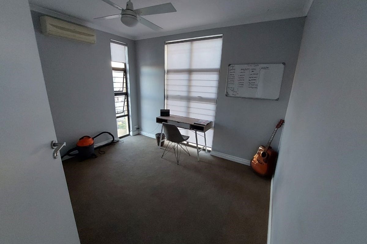 A functional bedroom featuring carpet flooring, a ceiling fan, and a wall-mounted split-system air conditioner, providing a comfortable and versatile living space.