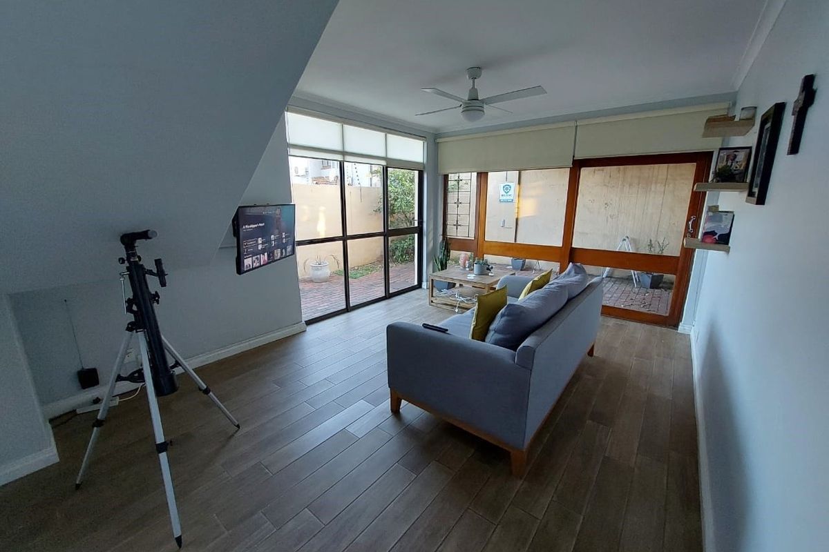 A bright living room featuring wood-look tiled flooring, a ceiling fan, and large sliding glass doors providing access to the outdoor area.