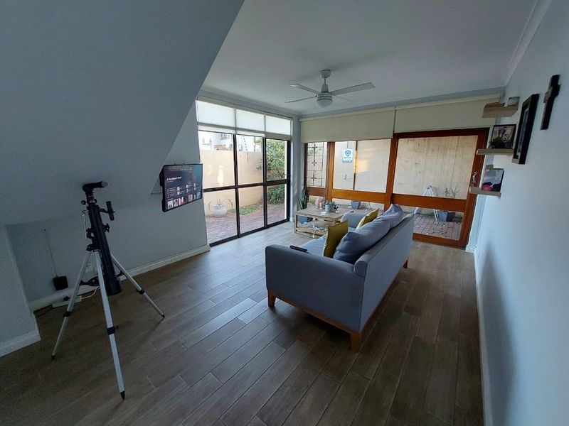 A bright living room featuring wood-look tiled flooring, a ceiling fan, and large sliding glass doors providing access to the outdoor area.