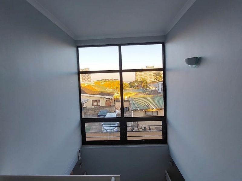 A bright, minimalist stairwell featuring a large window that provides natural light and views of the surrounding neighbourhood.
