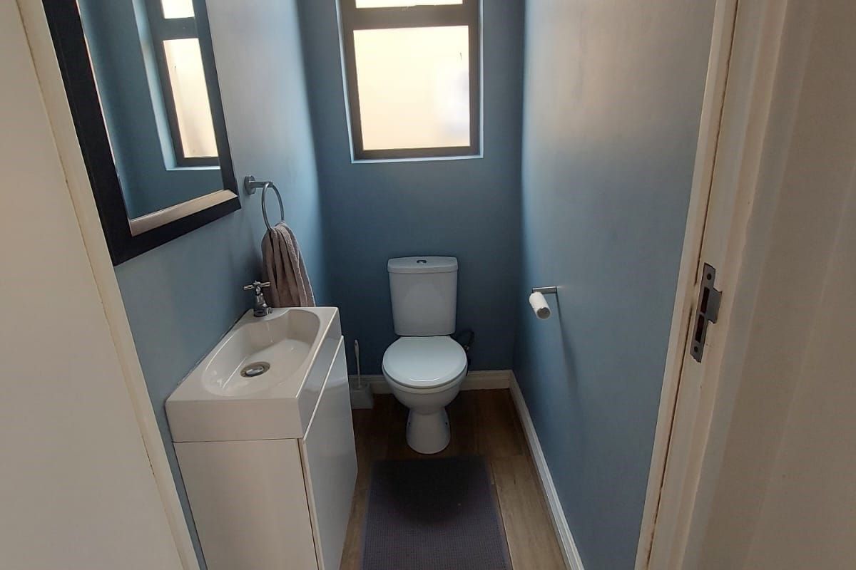 A compact guest bathroom featuring a modern vanity basin, toilet, and tiled flooring with a louvered window for ventilation.