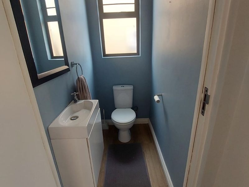 A compact guest bathroom featuring a modern vanity basin, toilet, and tiled flooring with a louvered window for ventilation.