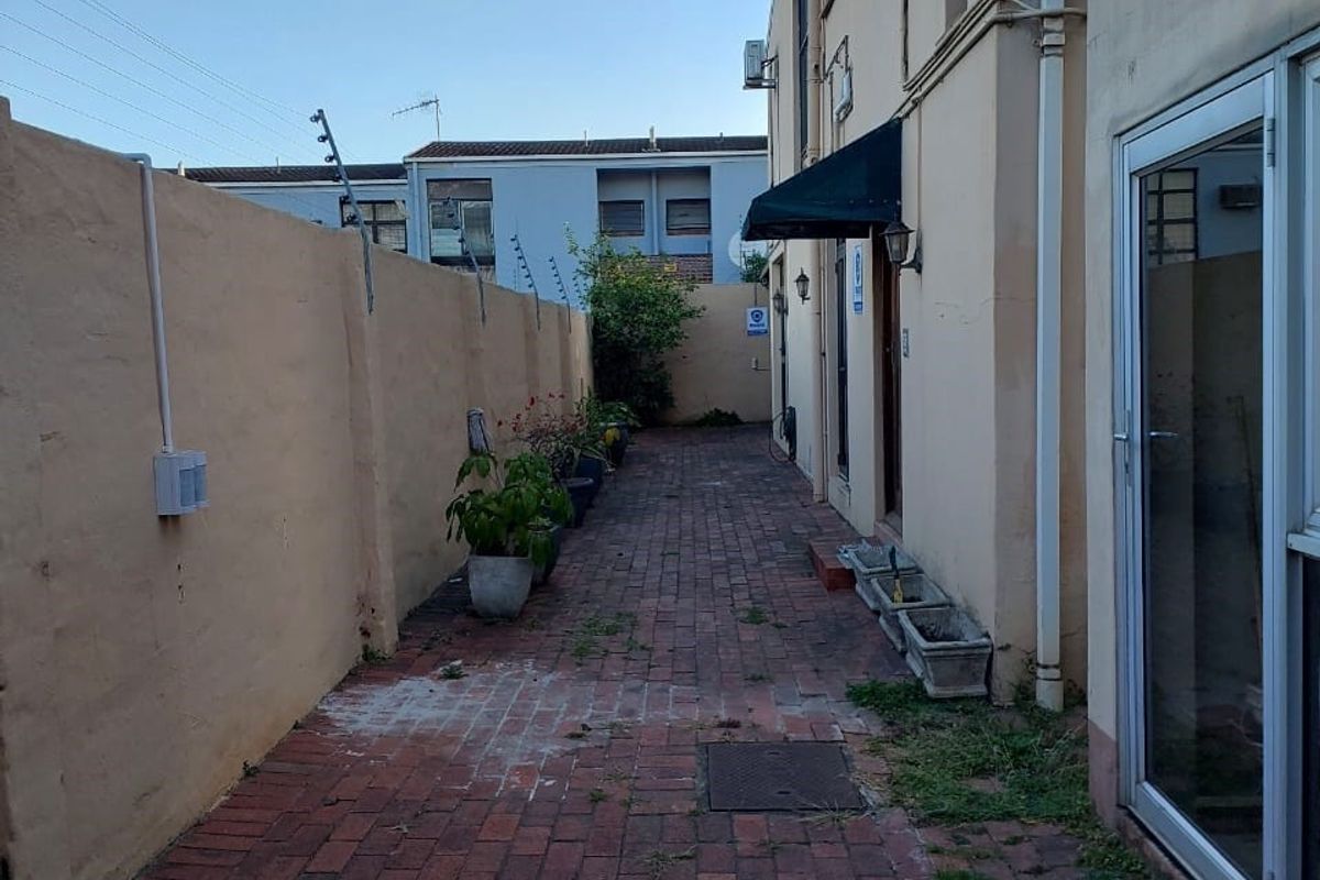 A side courtyard area featuring brick paving, a boundary wall with electric fencing, and an entrance awning, requiring some maintenance and landscaping.