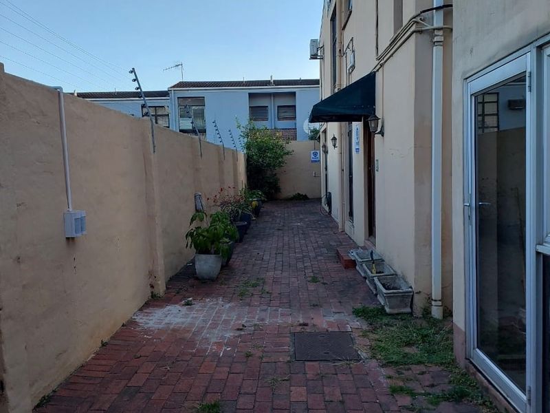 A side courtyard area featuring brick paving, a boundary wall with electric fencing, and an entrance awning, requiring some maintenance and landscaping.