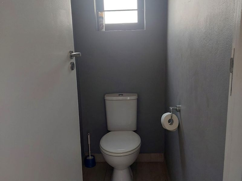 A compact guest toilet featuring tiled flooring, a louvered window for ventilation, and a modern grey wall finish.