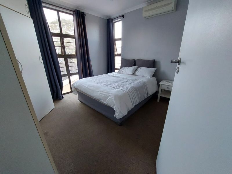 A functional bedroom featuring carpeted flooring, built-in wardrobe storage, and a wall-mounted split-system air conditioning unit.