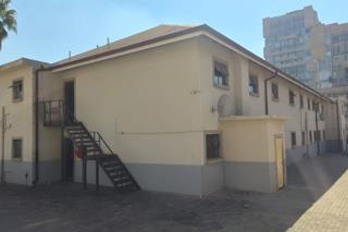 Rear exterior view of the apartment building featuring a metal staircase, paved courtyard area, and multi-level window placements.