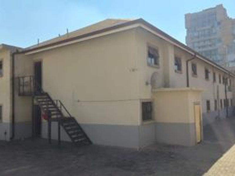 Rear exterior view of the apartment building featuring a metal staircase, paved courtyard area, and multi-level window placements.
