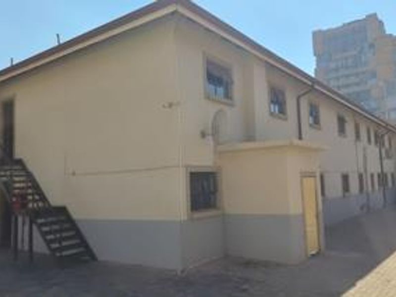 Rear exterior view of the apartment building featuring a paved courtyard, external metal staircase, and security-fitted windows.