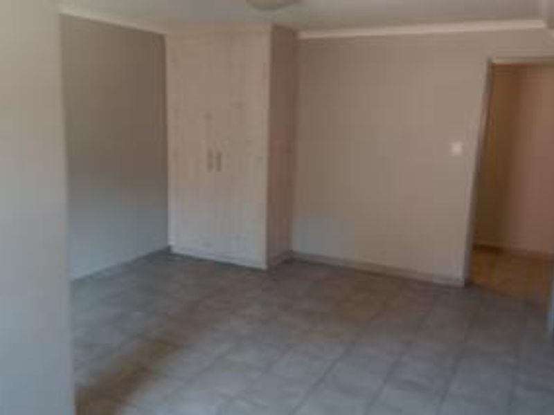 An empty bedroom featuring neutral wall paint, tiled flooring, and built-in cupboards, offering a clean and versatile space.