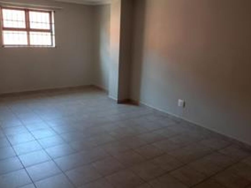 An empty, neutrally painted living area featuring tiled flooring and a window fitted with security bars.