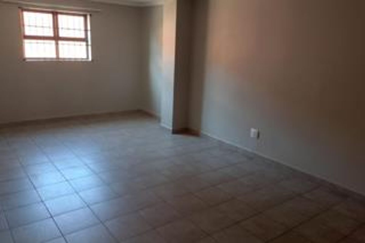An empty, neutrally painted living area featuring tiled flooring and a window fitted with security bars.