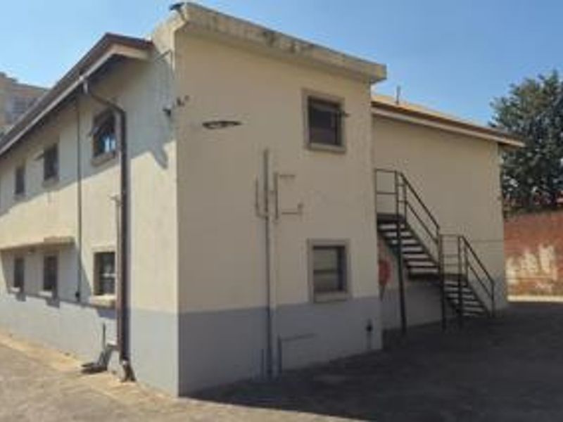Rear view of the apartment building featuring an external staircase, paved yard area, and functional exterior lighting.