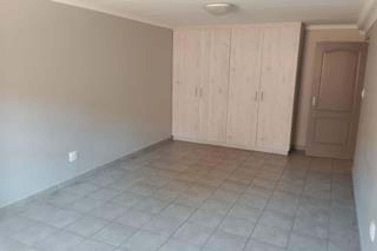 A spacious, empty bedroom featuring neutral wall tones, tiled flooring, and ample built-in cupboard storage.