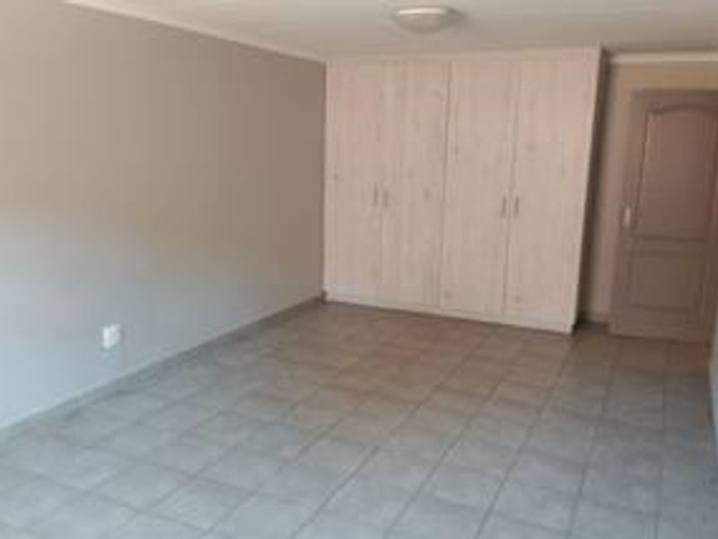 A spacious, empty bedroom featuring neutral wall tones, tiled flooring, and ample built-in cupboard storage.