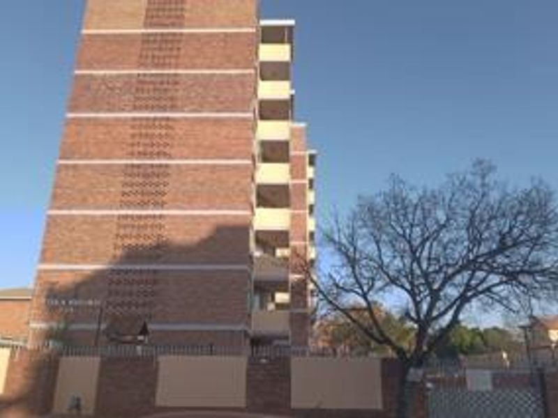Exterior view of a multi-story brick apartment building featuring private balconies and a secure perimeter wall.