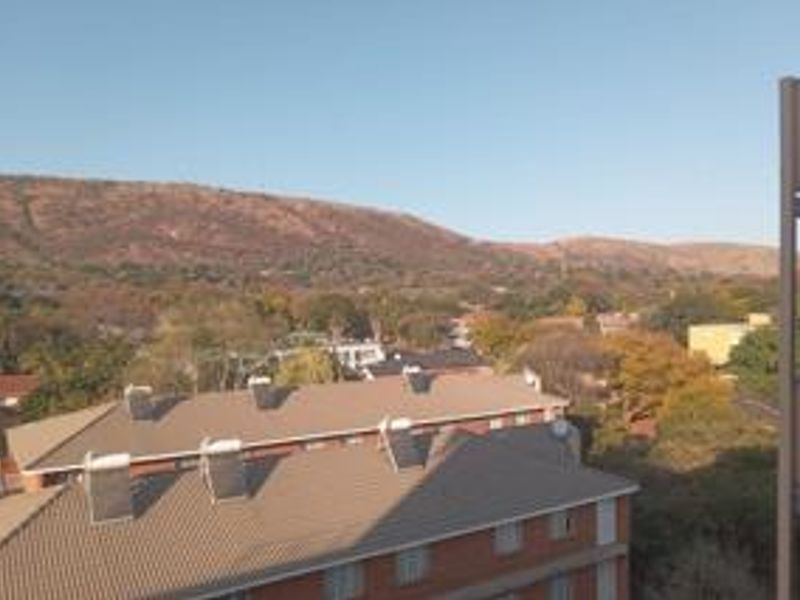Elevated view overlooking surrounding residential buildings with solar water heating panels and scenic mountain backdrop.