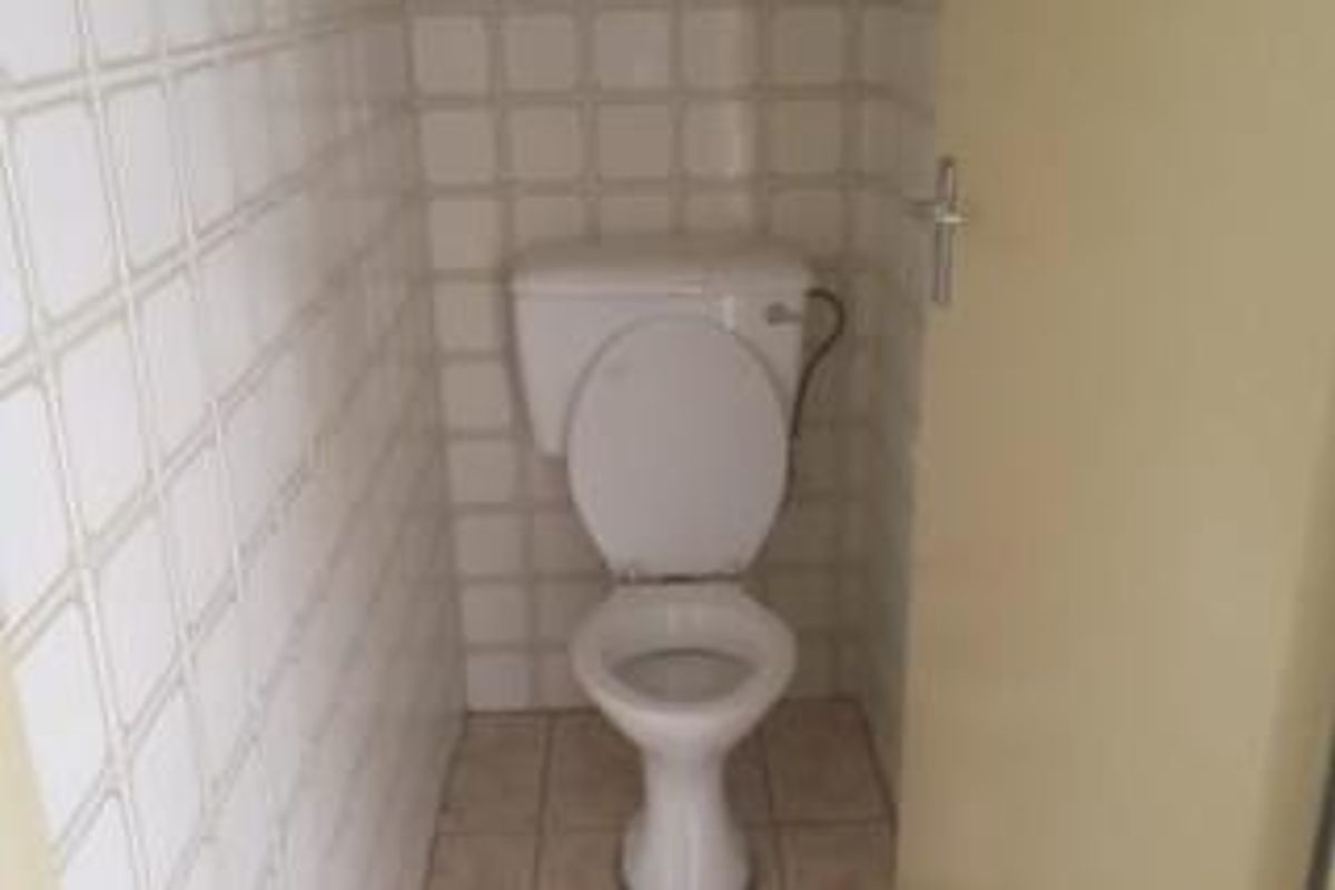 A compact, functional bathroom featuring a standard toilet with tiled walls and flooring, presenting a dated aesthetic in need of modernization.