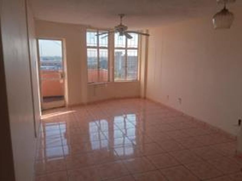 An empty, sunlit living area featuring tiled floors, a ceiling fan, and direct access to a balcony through a glass door.