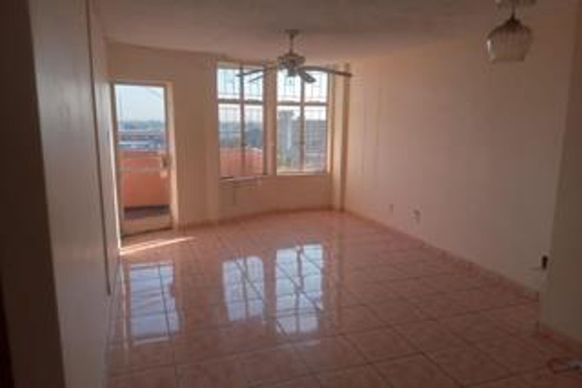 An empty, sunlit living area featuring tiled floors, a ceiling fan, and direct access to a balcony through a glass door.