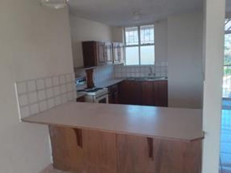 A dated kitchen featuring wooden cabinetry, laminate countertops, a breakfast bar, and tiled flooring, offering a functional layout with potential for modernization.