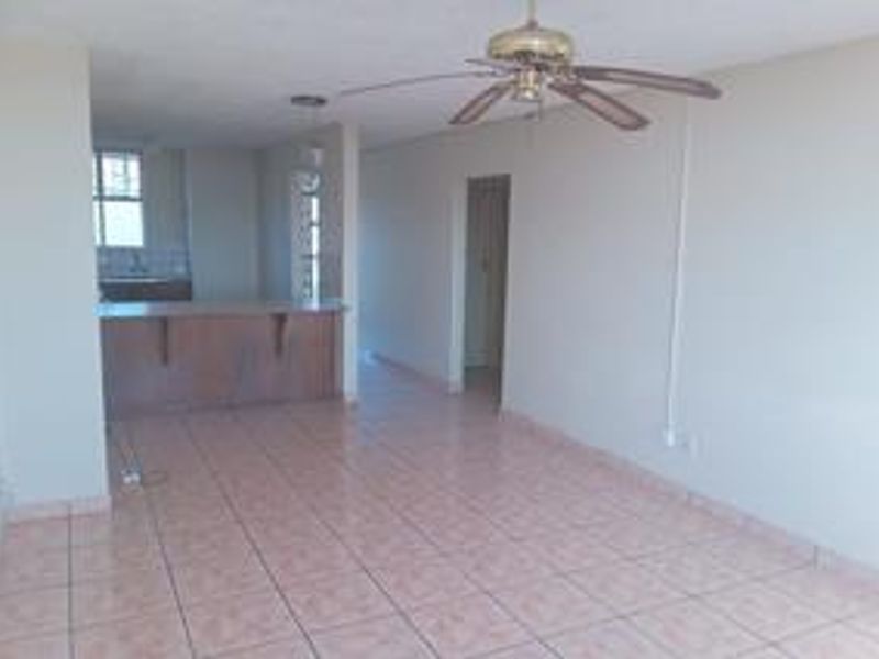 Spacious open-plan living area featuring tiled flooring, a ceiling fan, and an integrated breakfast bar connecting to the kitchen space.