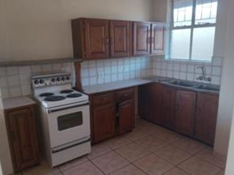A functional kitchen featuring wooden cabinetry, tiled backsplash, double sink, and a freestanding stove, offering a dated but practical layout for renovation.