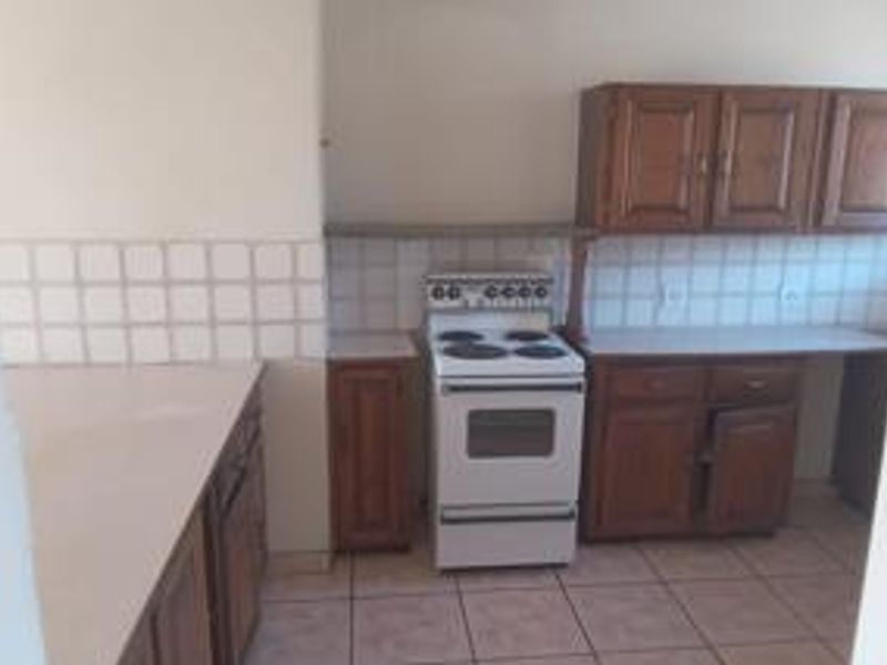 A dated kitchen featuring wooden cabinetry, tiled backsplash, and tiled flooring, providing a functional space ready for modernization.