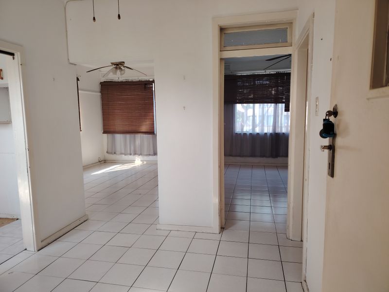 A bright, vacant hallway featuring white tiled flooring and multiple doorways leading into adjacent living spaces with ceiling fans.