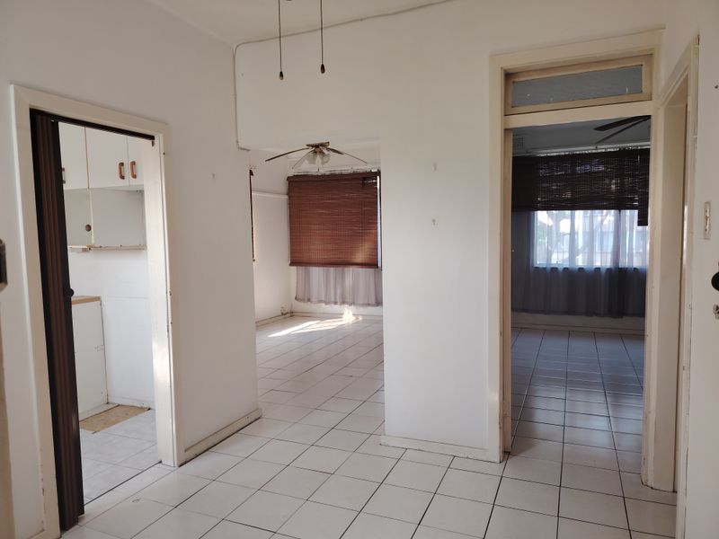 A central hallway with tiled flooring providing access to multiple rooms, including a kitchen and living areas, featuring neutral walls and ceiling fans.
