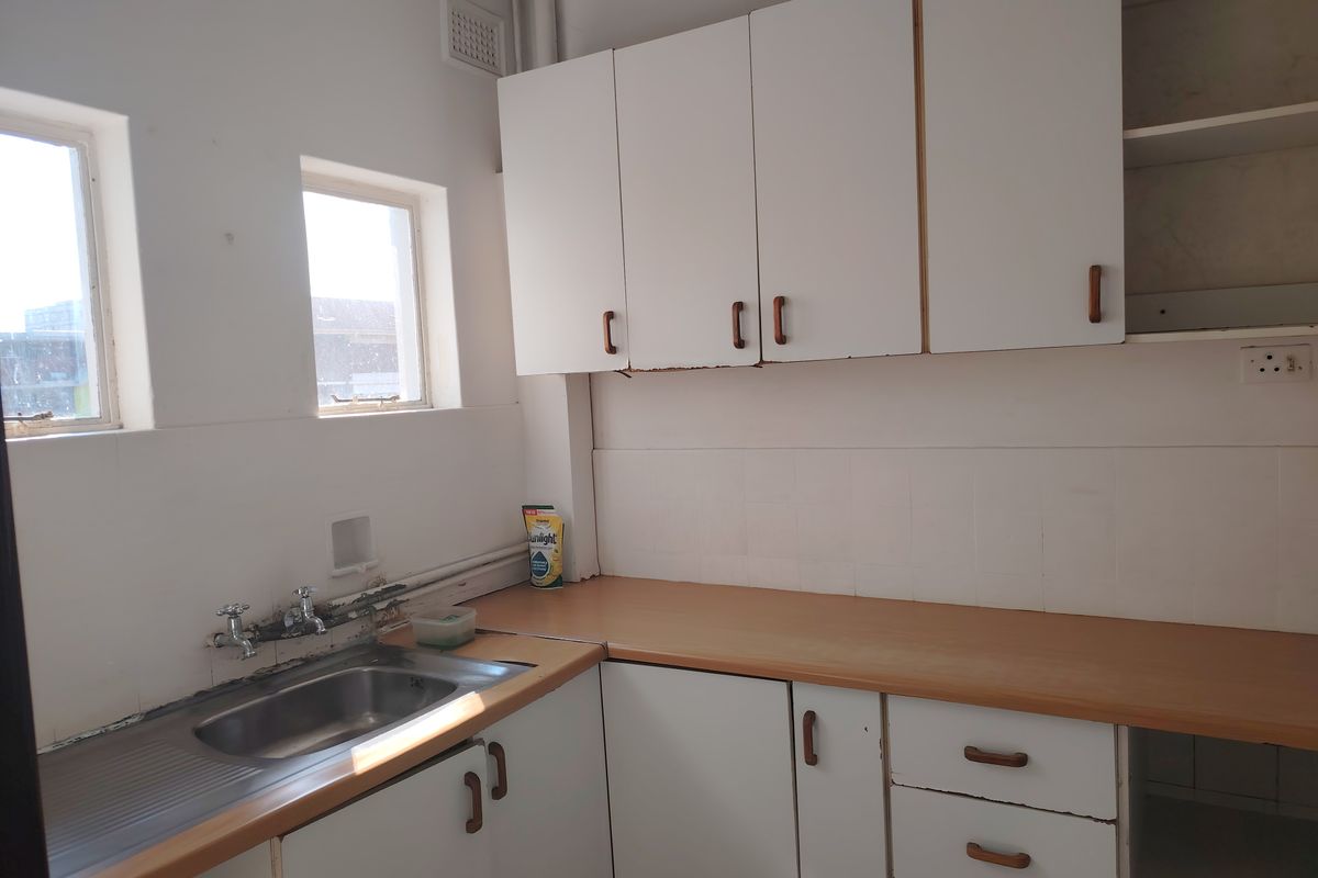 A dated kitchen featuring white built-in cabinetry, a laminate countertop, and a stainless steel sink with tiled backsplash.