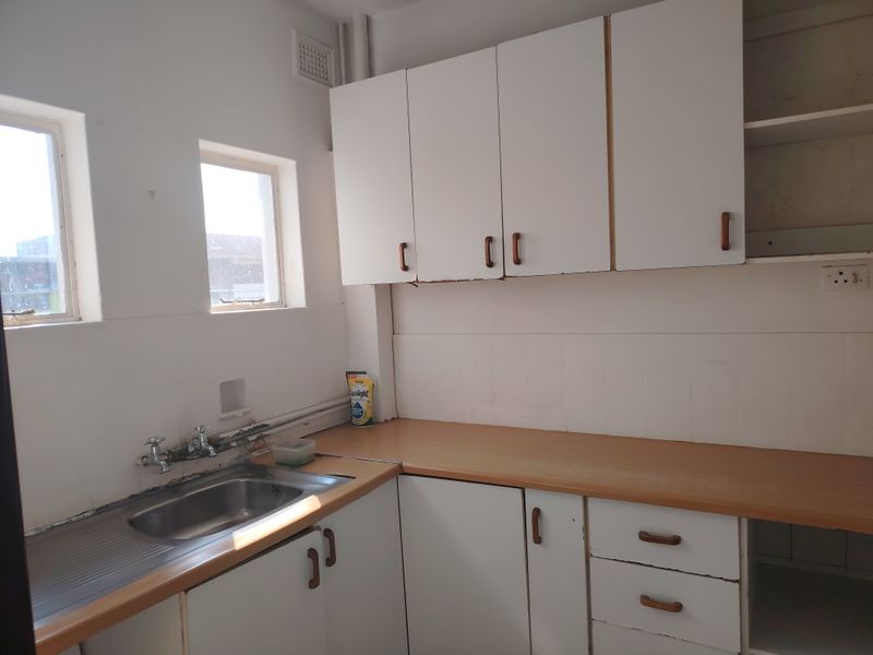 A dated kitchen featuring white built-in cabinetry, a laminate countertop, and a stainless steel sink with tiled backsplash.