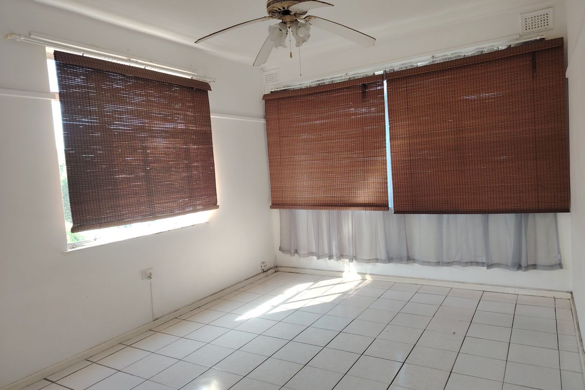 An empty bedroom featuring white tiled flooring, a ceiling fan, and window blinds, offering a clean and neutral space ready for personalization.