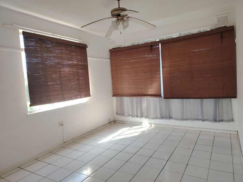 An empty bedroom featuring white tiled flooring, a ceiling fan, and window blinds, offering a clean and neutral space ready for personalization.